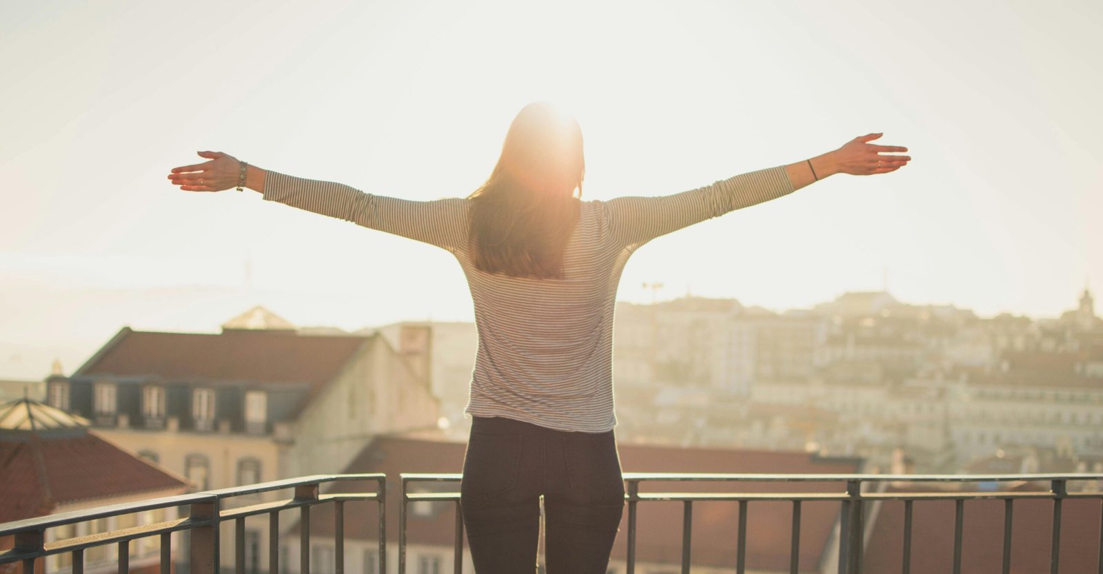 Services A woman stands with outstretched arms on a sunny balcony, embracing the morning light.
